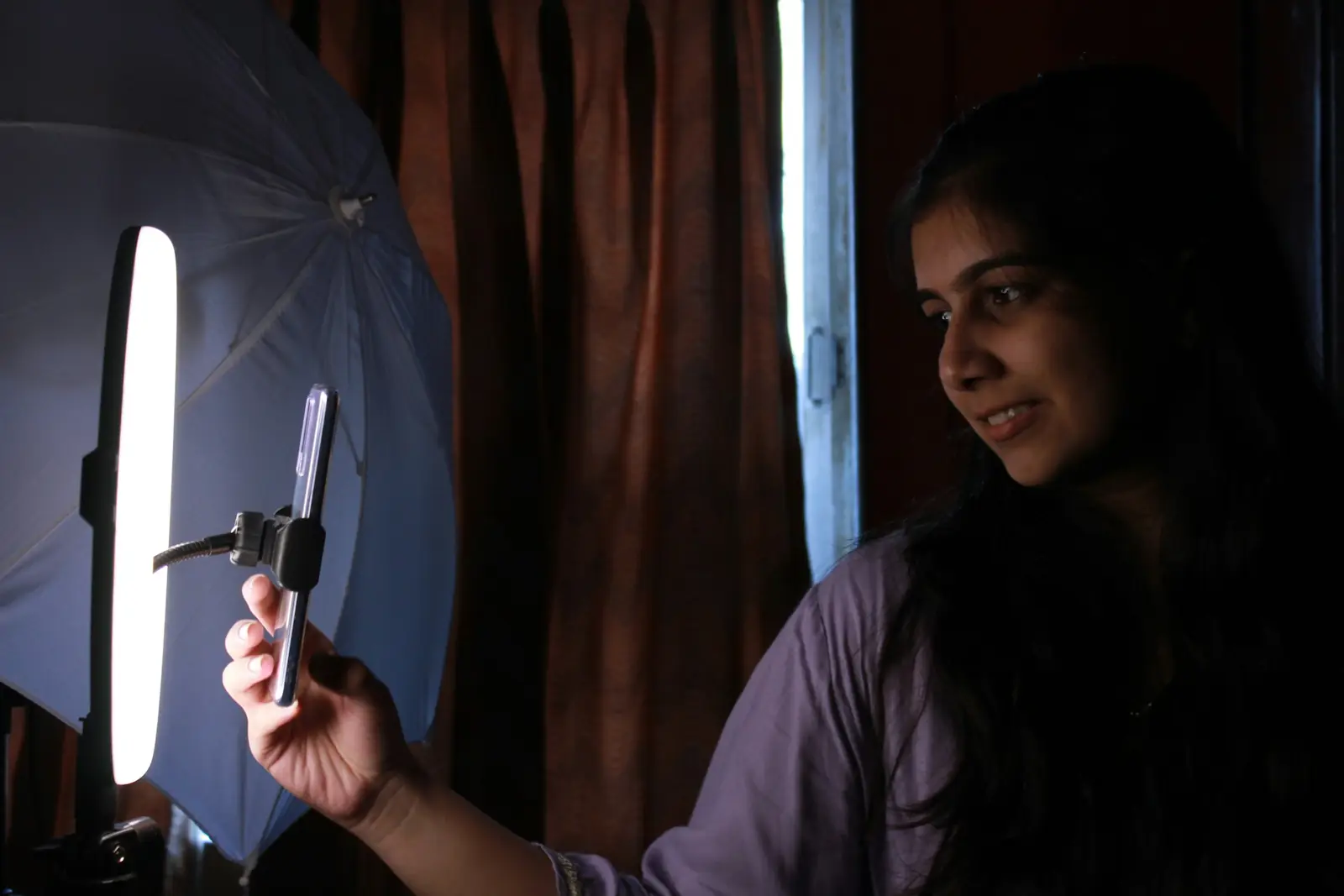 A young woman filming herself on a smartphone in front of a ring light