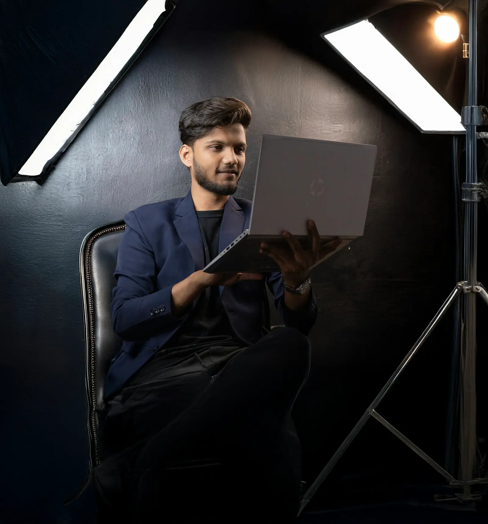 A young man working on a laptop in a small studio lit by softbox lights