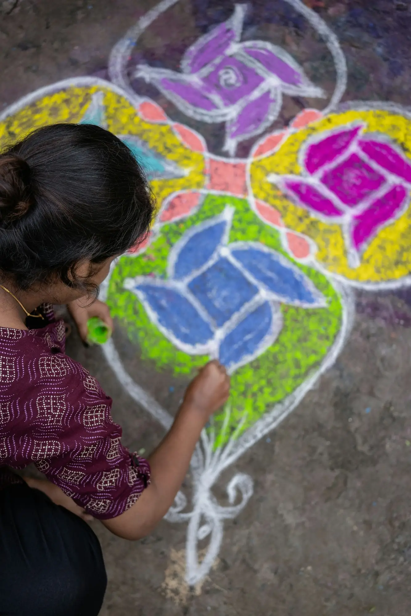 A woman drawing a colourful kolam on the ground in Tamil Nadu