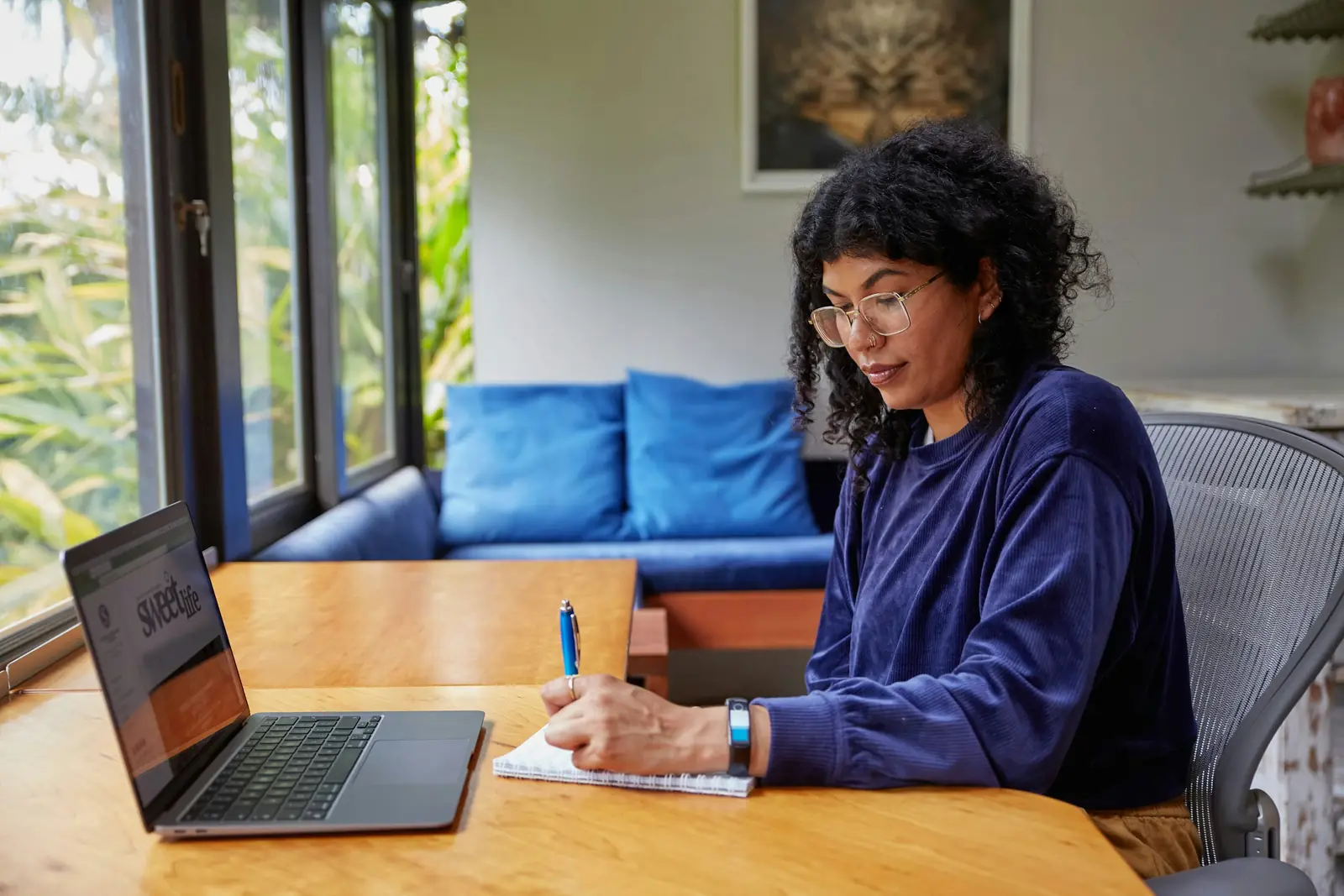 A woman working on a laptop and taking notes at a wooden table